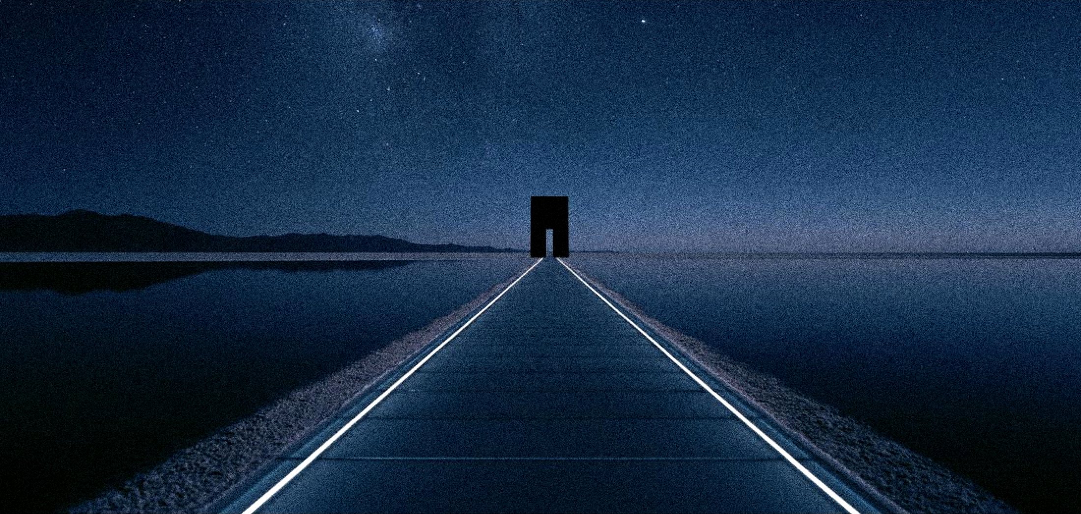 A long glass causeway across a calm dark lake to a monolith gateway under a deep starfield